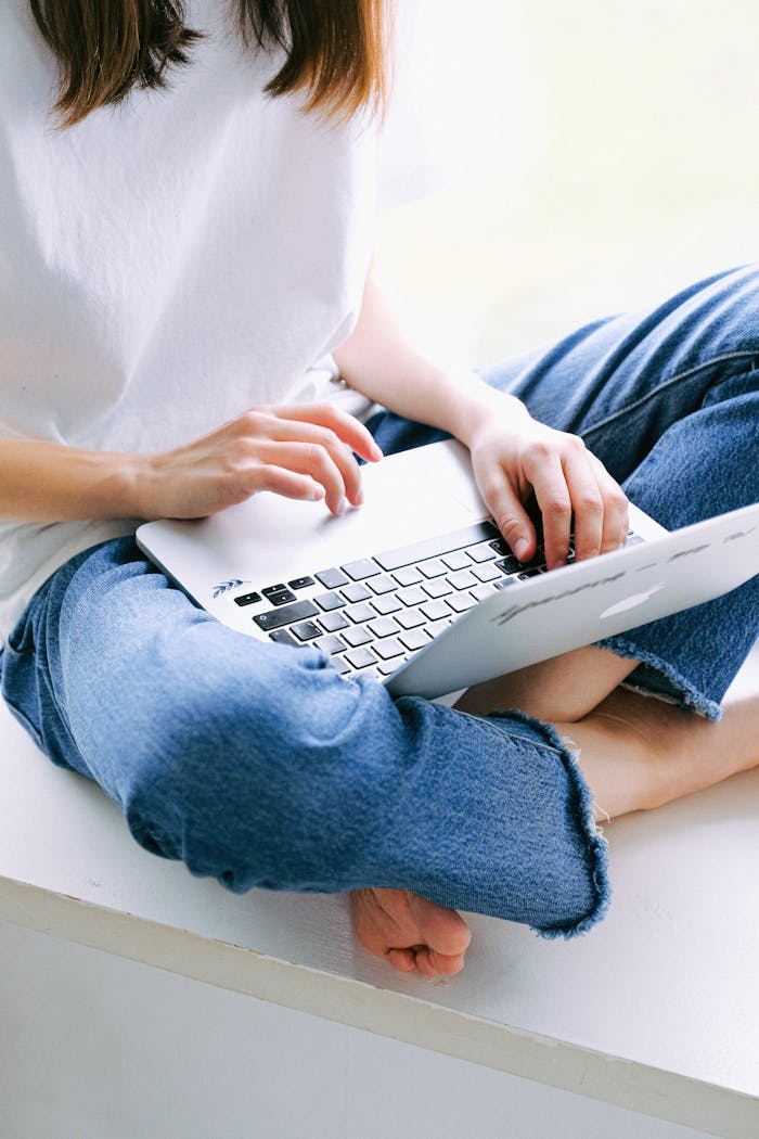 who-we-are Woman sitting cross-legged in casual jeans working on a laptop indoors.