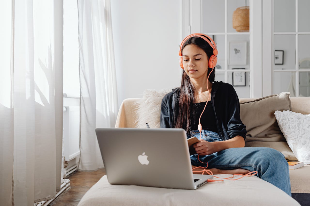 services-01 Teenage girl wearing headphones using a laptop for online learning at home in a cozy setting.